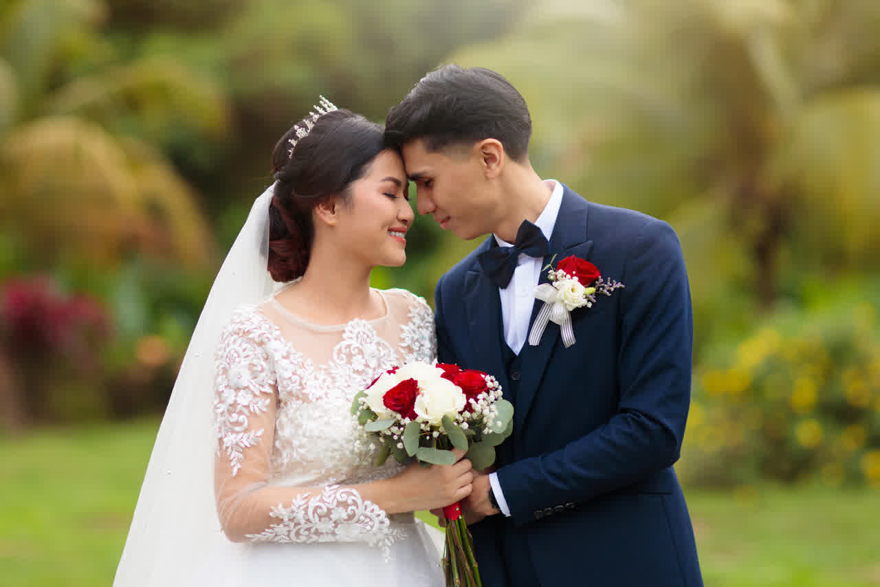 Pareja de novios abrazada durante la sesión de fotos de su boda, con un ramo de rosas rojas y blancas