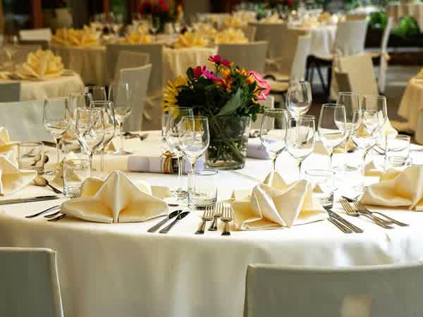 Mesas redondas con mantelería, servilletas dobladas, cristalería y un centro de flores, montadas para una recepción